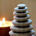 Piedras de spa, una vela encendida y un cuenco con hierbas de lavanda para una noche de relajación.